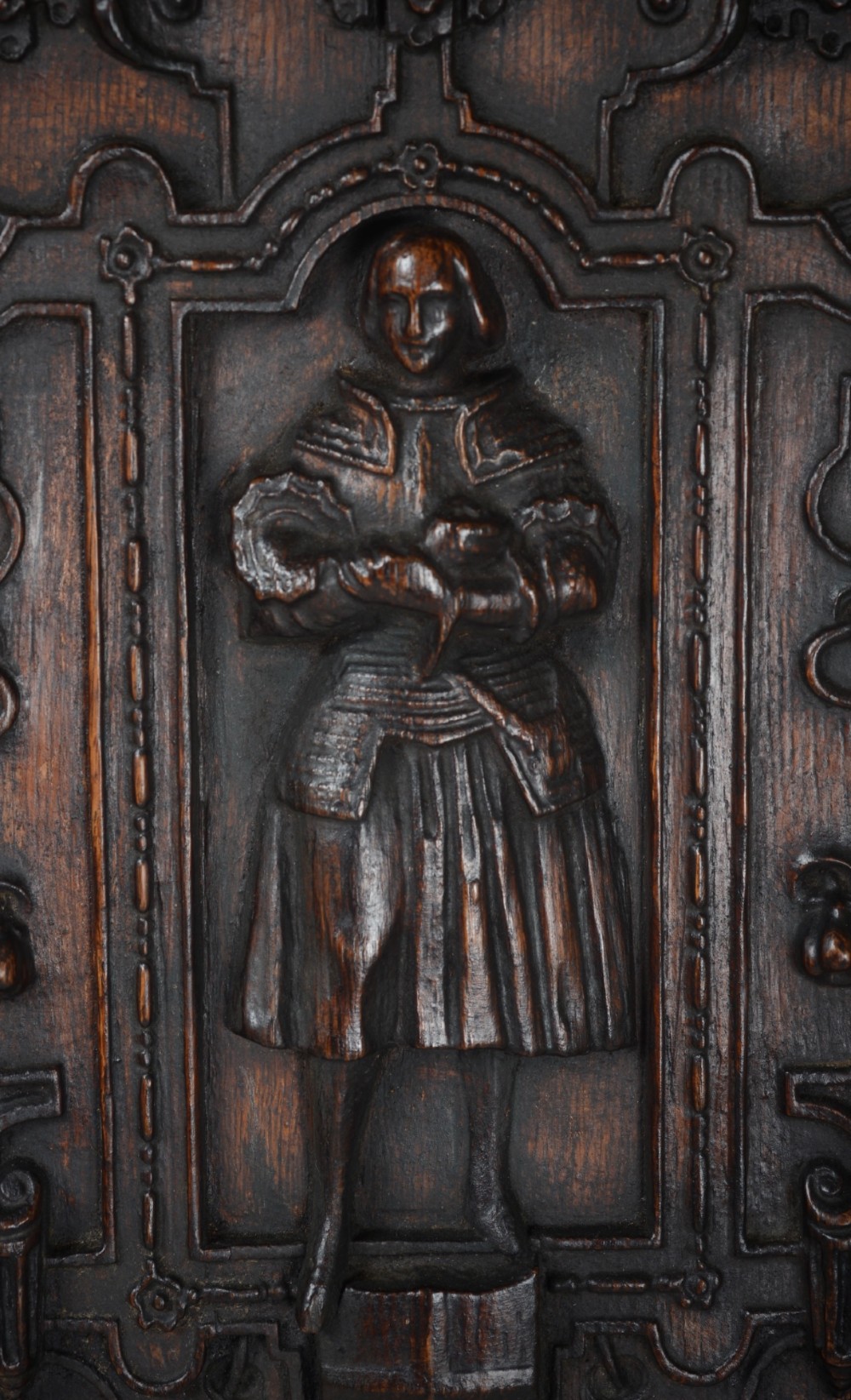 A dark brown rectangular carved oak panel depicting a central relief figure in armour framed by intricate strapwork and decorative scrollwork. View V