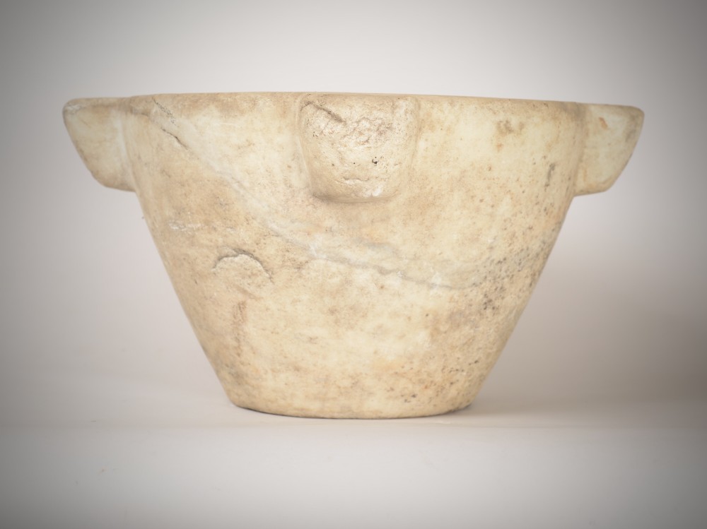 A large, hand-carved off-white marble mortar featuring tapered sides and prominent carved side lugs.