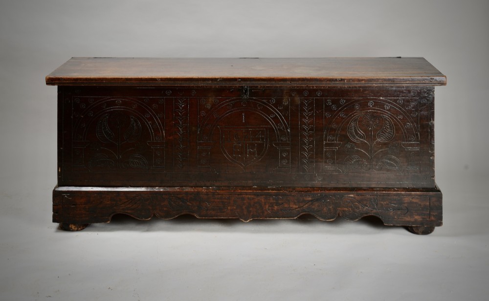A dark brown 17th-century carved oak coffer featuring three carved arch panels, a central shield panel inscribed with the date 1644, and a shaped lower apron.