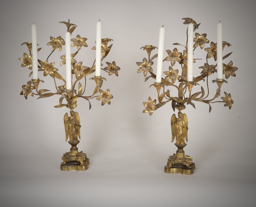A pair of gilt brass Gothic Revival candelabra featuring sculpted angel pedestal bases and branching lily arms holding candles.