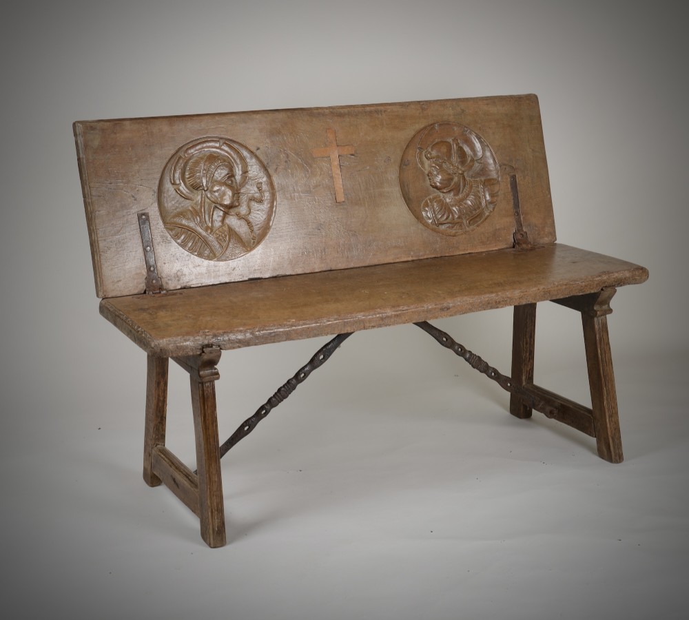 A Renaissance style carved wooden bench featuring two profile portrait roundels flanking a central cross on the backrest and wrought iron support stretchers beneath.