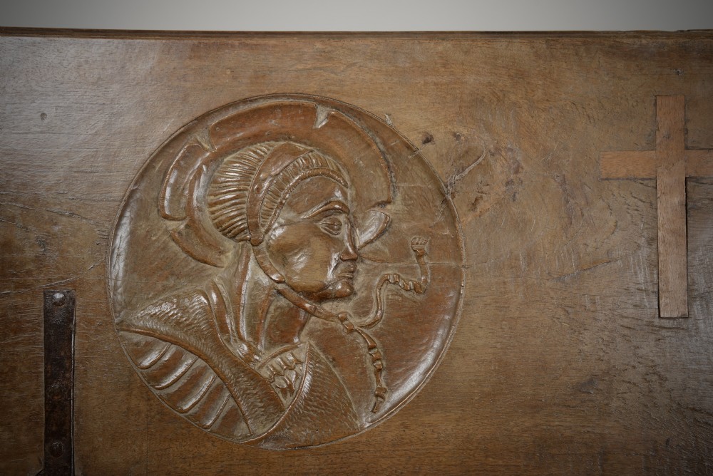 A Renaissance style carved wooden bench featuring two profile portrait roundels flanking a central cross on the backrest and wrought iron support stretchers beneath. View V