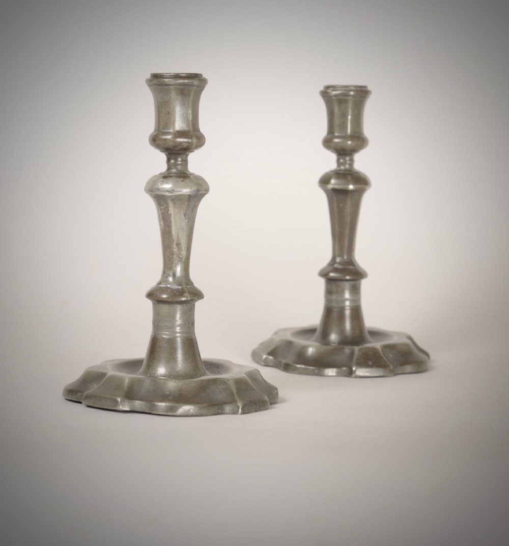 A pair of 18th-century pewter candlesticks featuring baluster stems and shaped scalloped bases.