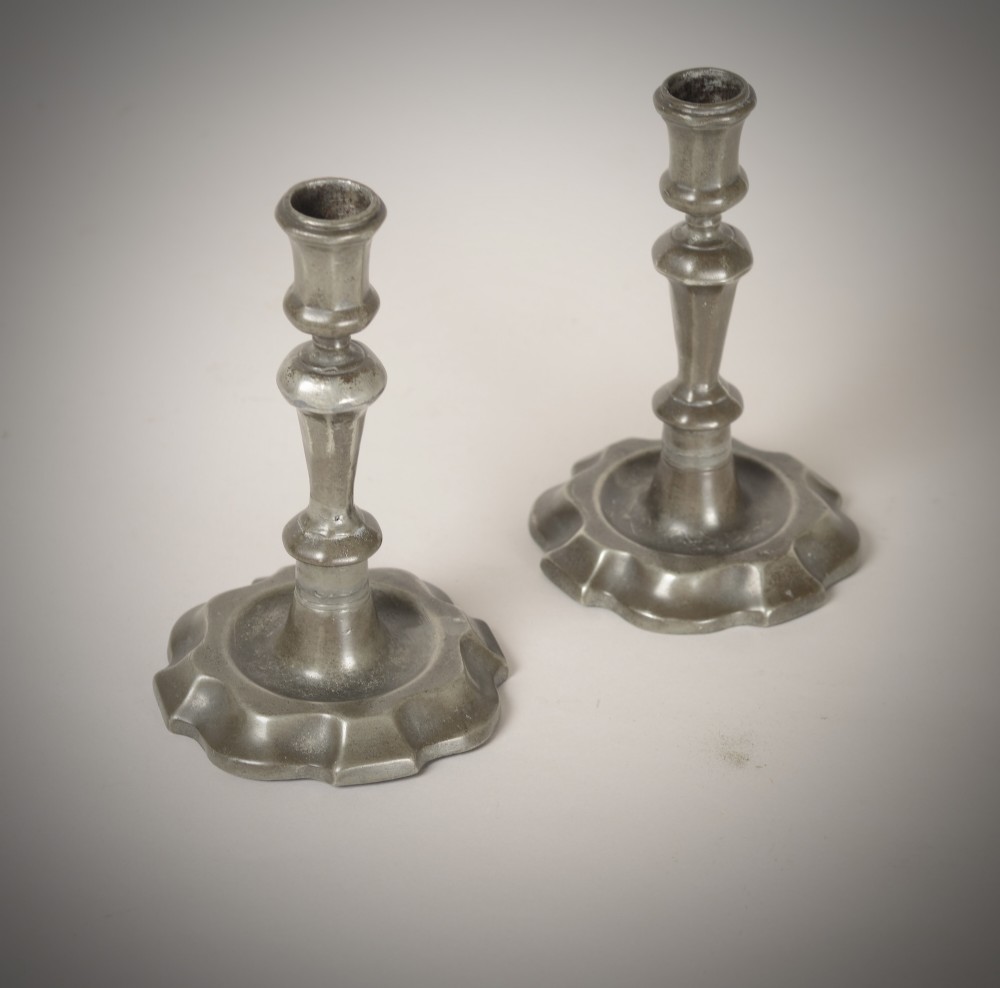 A pair of 18th-century pewter candlesticks featuring baluster stems and shaped scalloped bases. View V