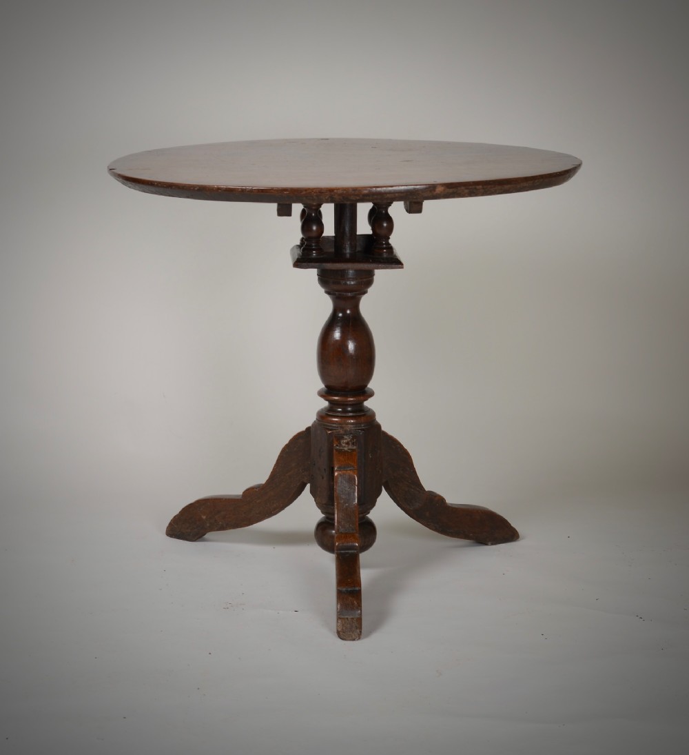An antique dark brown oak tripod table featuring a circular top, a birdcage support mechanism, a turned central column, and three splayed feet.