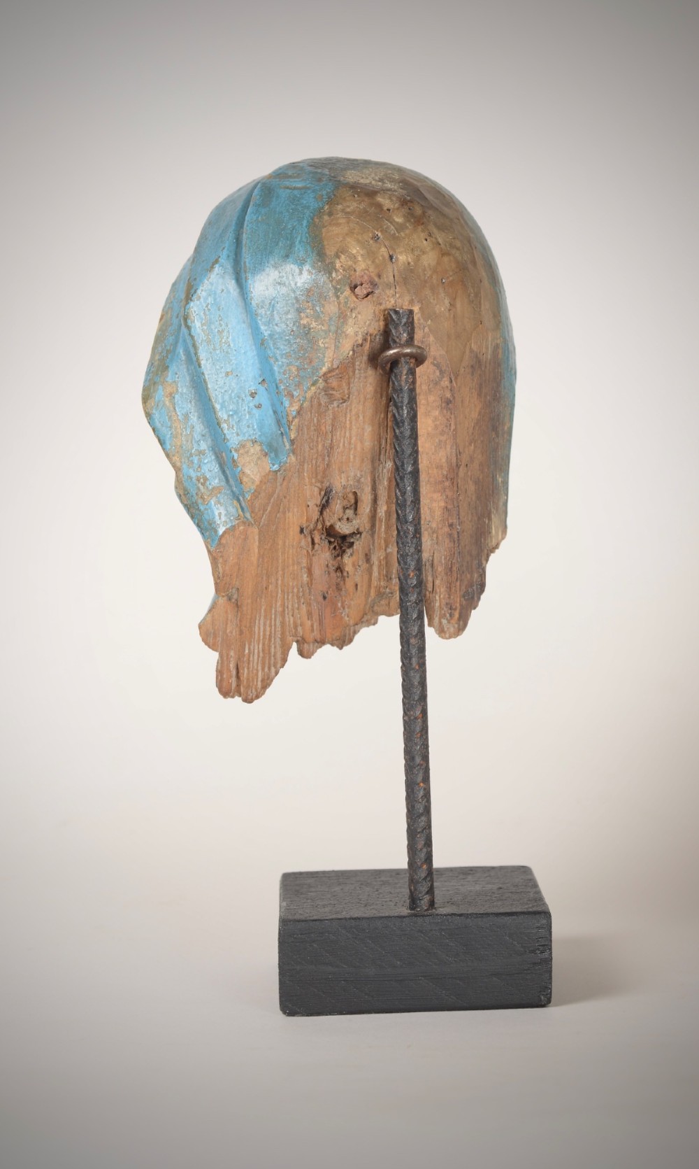 A 17th-century carved wooden head fragment of the Virgin Mary featuring polychrome blue and gold headwear, mounted on a slim black metal rod and square base. View III