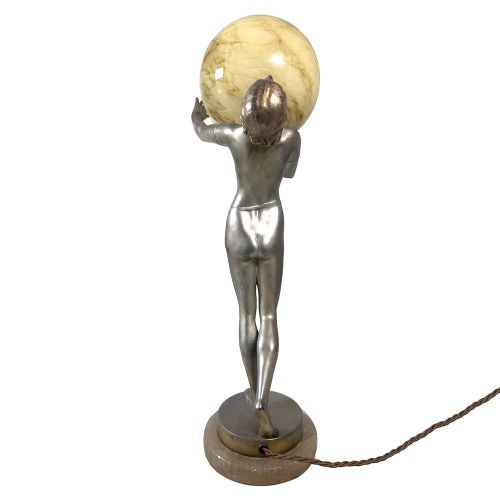 An Art Deco spelter table lamp featuring a silvered female figure holding up an amber glass globe shade on a circular onyx base. View VIII
