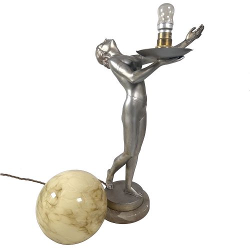 An Art Deco spelter table lamp featuring a silvered female figure holding up an amber glass globe shade on a circular onyx base. View IX