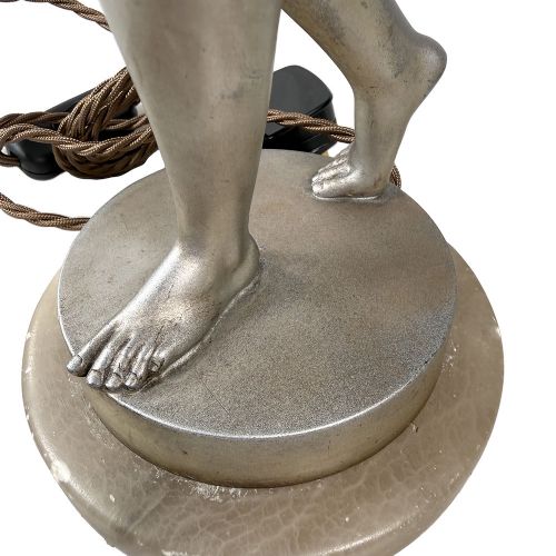 An Art Deco spelter table lamp featuring a silvered female figure holding up an amber glass globe shade on a circular onyx base. View XII