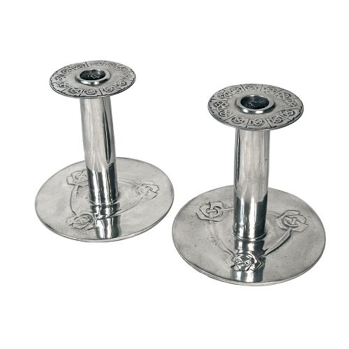 A pair of silver-tone pewter candlesticks featuring tapered cylindrical stems, flat wide sconces, and broad circular bases decorated with relief stylised plant motifs. View II