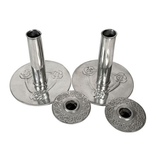 A pair of silver-tone pewter candlesticks featuring tapered cylindrical stems, flat wide sconces, and broad circular bases decorated with relief stylised plant motifs. View IV