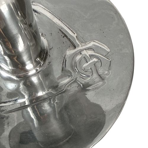 A pair of silver-tone pewter candlesticks featuring tapered cylindrical stems, flat wide sconces, and broad circular bases decorated with relief stylised plant motifs. View V