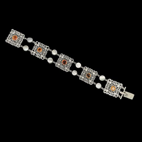 An Arts and Crafts period silver link bracelet featuring intricate openwork square panels set with central round orange citrines, connected by paired circular blister pearls. View IV