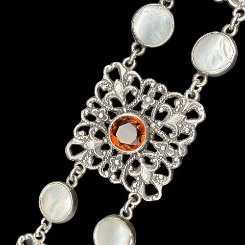 An Arts and Crafts period silver link bracelet featuring intricate openwork square panels set with central round orange citrines, connected by paired circular blister pearls. View V