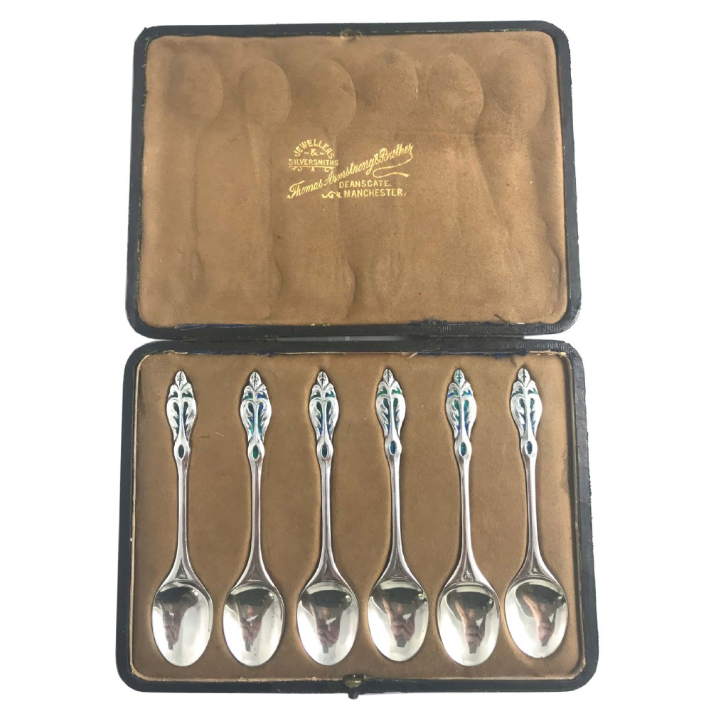 A set of six silver Arts and Crafts spoons featuring blue and green enamelled handles, arranged inside an open presentation box with a brown lining. View II