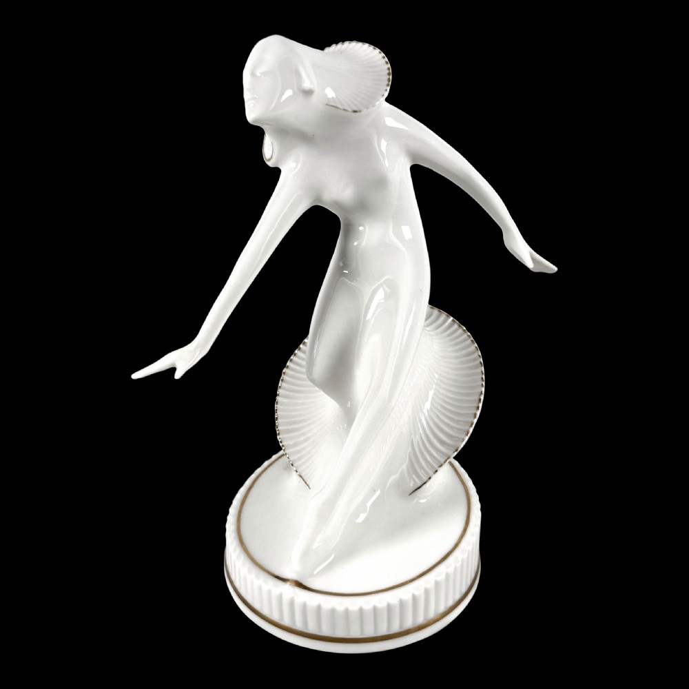 A white glazed porcelain Art Deco figurine depicting a female dancer in dynamic motion with pleated gold-trimmed drapery on a circular base. View II