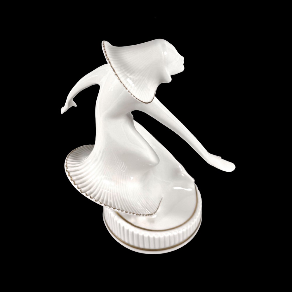 A white glazed porcelain Art Deco figurine depicting a female dancer in dynamic motion with pleated gold-trimmed drapery on a circular base. View III