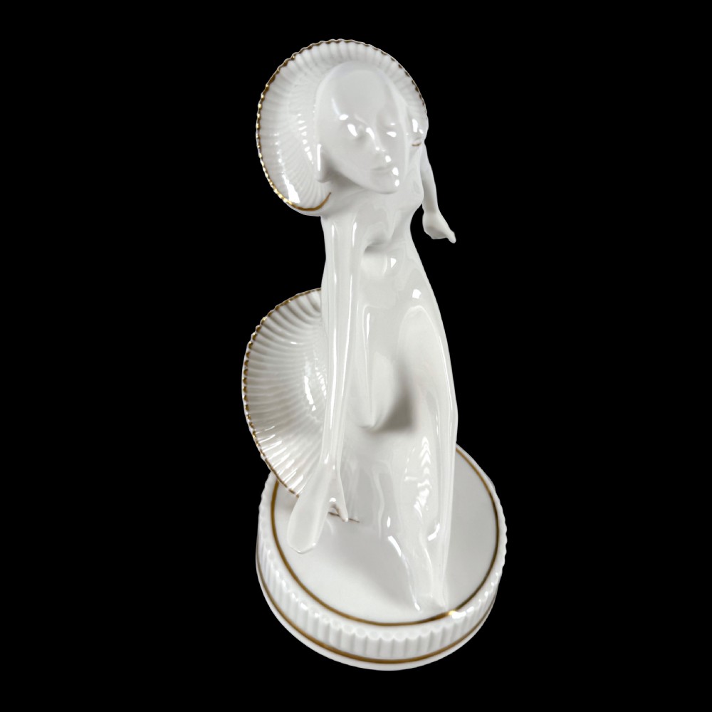 A white glazed porcelain Art Deco figurine depicting a female dancer in dynamic motion with pleated gold-trimmed drapery on a circular base. View V