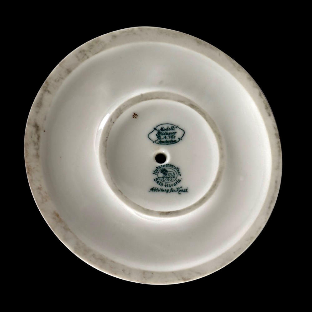 A white glazed porcelain Art Deco figurine depicting a female dancer in dynamic motion with pleated gold-trimmed drapery on a circular base. View VI