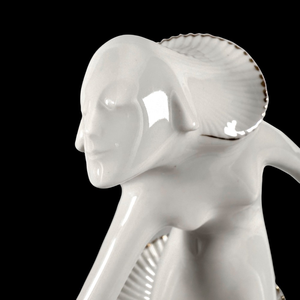 A white glazed porcelain Art Deco figurine depicting a female dancer in dynamic motion with pleated gold-trimmed drapery on a circular base. View VIII