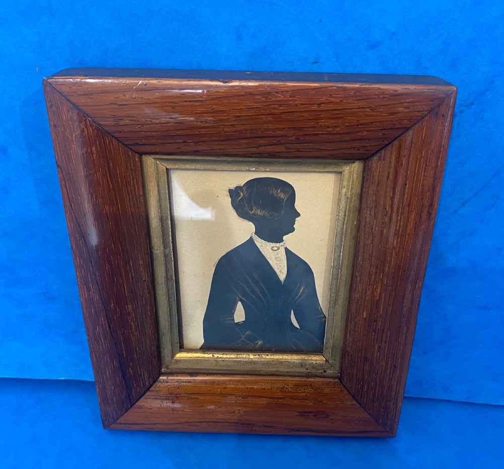 A Victorian profile silhouette portrait of a woman with detailed bronzed hair and collar, framed in a wide rosewood frame with a gilded inner slip.