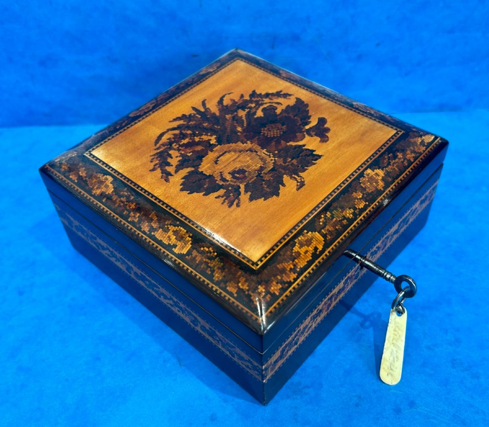 A square Victorian wooden box featuring a central floral mosaic inlay panel, detailed geometric mosaic borders, and a metal key. View V