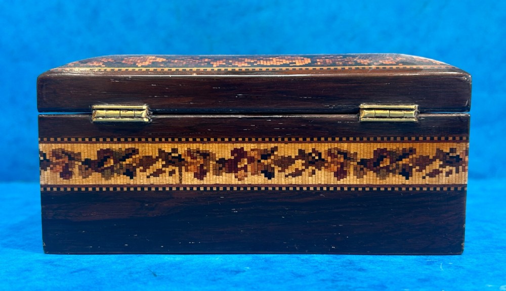 A square Victorian wooden box featuring a central floral mosaic inlay panel, detailed geometric mosaic borders, and a metal key. View VII