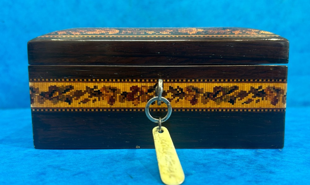 A square Victorian wooden box featuring a central floral mosaic inlay panel, detailed geometric mosaic borders, and a metal key. View IX