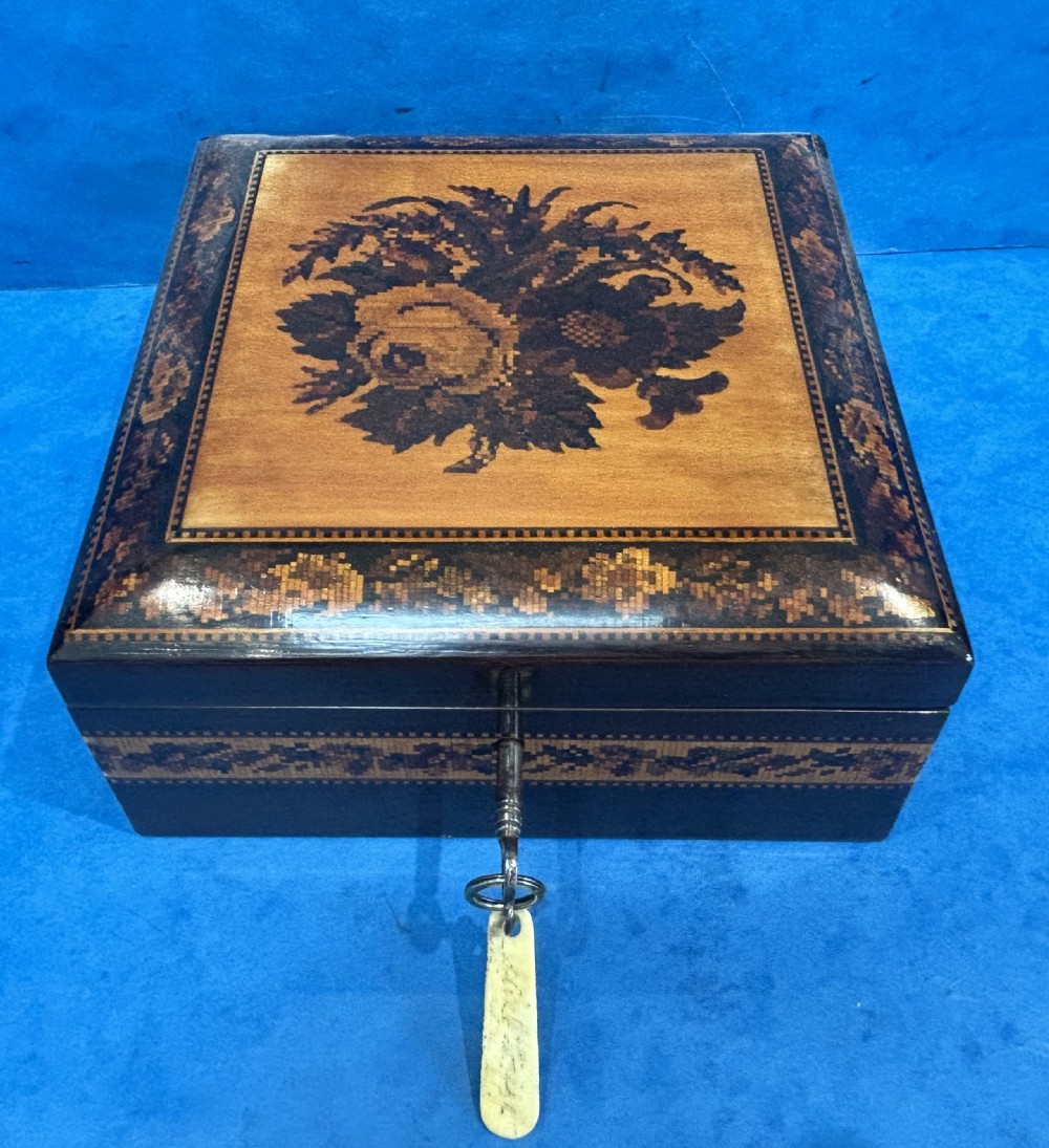 A square Victorian wooden box featuring a central floral mosaic inlay panel, detailed geometric mosaic borders, and a metal key. View XII