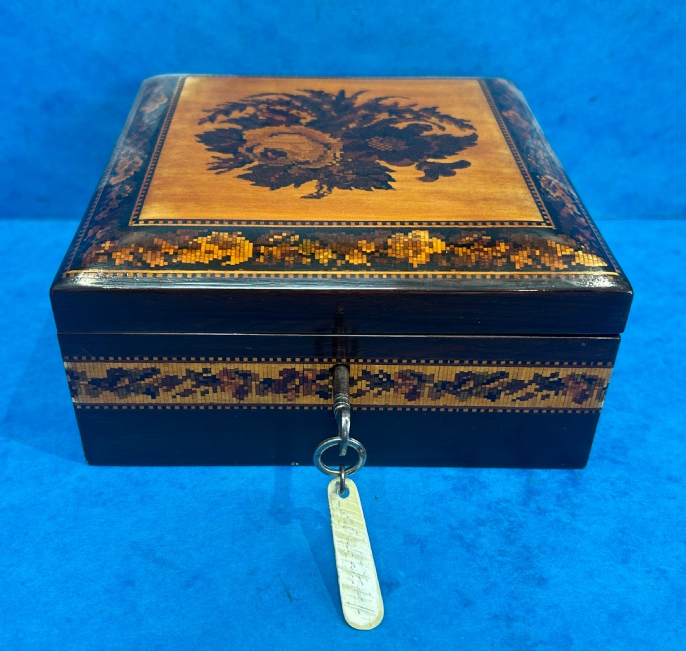 A square Victorian wooden box featuring a central floral mosaic inlay panel, detailed geometric mosaic borders, and a metal key. View XIII