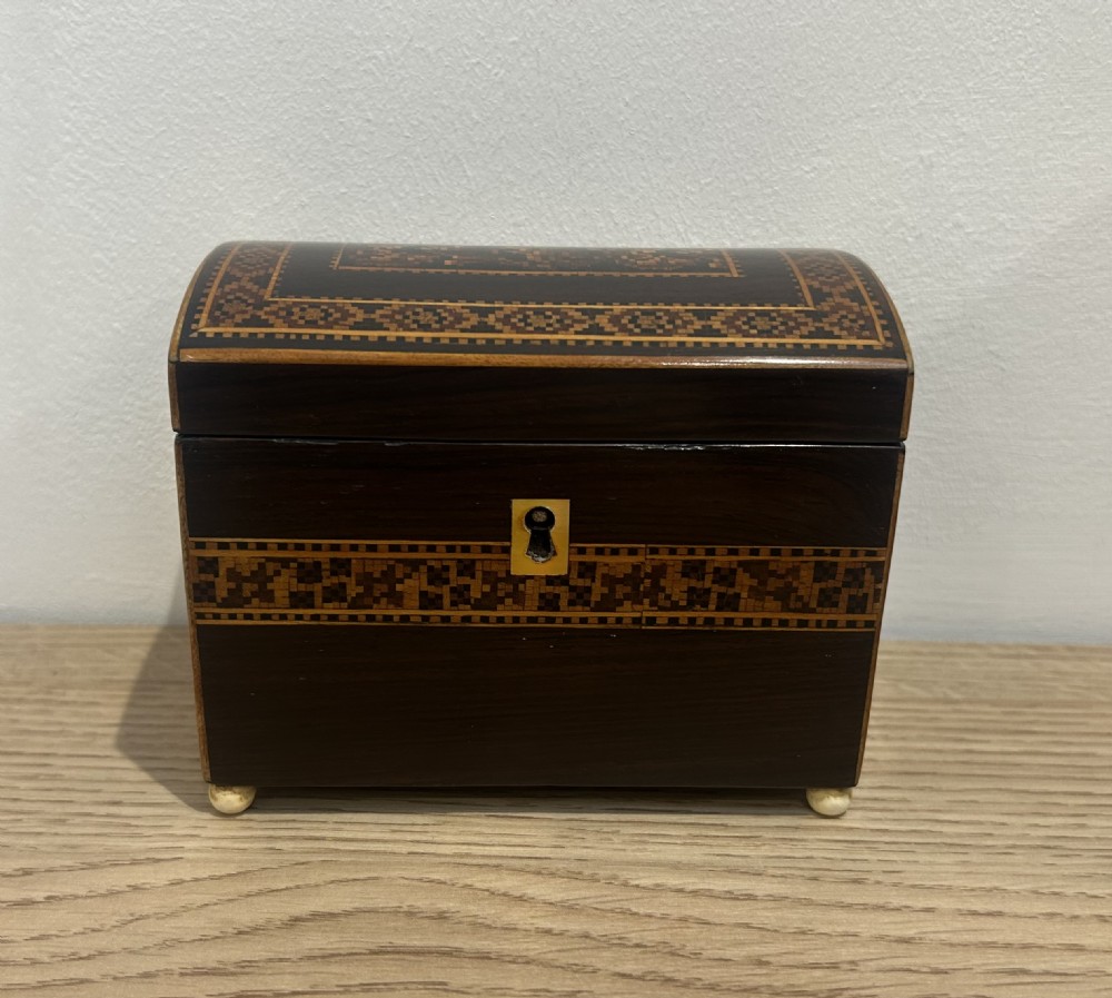 A Victorian rosewood tea caddy featuring a domed lid, geometric mosaic wood inlay, and a brass keyhole escutcheon. View II