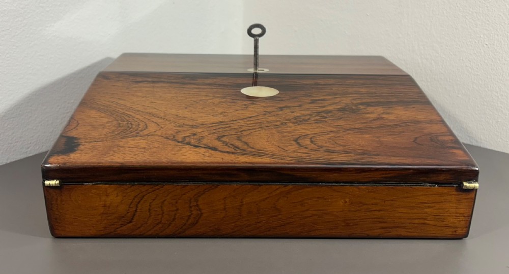 A William IV rosewood lap desk featuring a brass keyhole escutcheon with key inserted and a circular brass inlay on its sloped lid. View IV