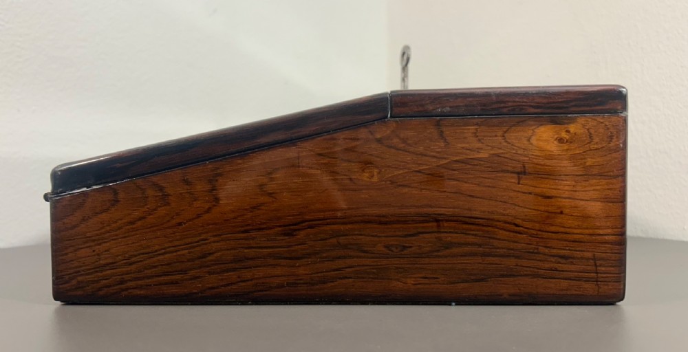 A William IV rosewood lap desk featuring a brass keyhole escutcheon with key inserted and a circular brass inlay on its sloped lid. View V