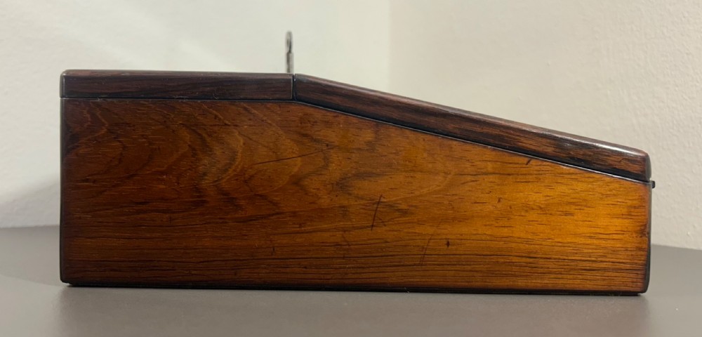 A William IV rosewood lap desk featuring a brass keyhole escutcheon with key inserted and a circular brass inlay on its sloped lid. View VIII
