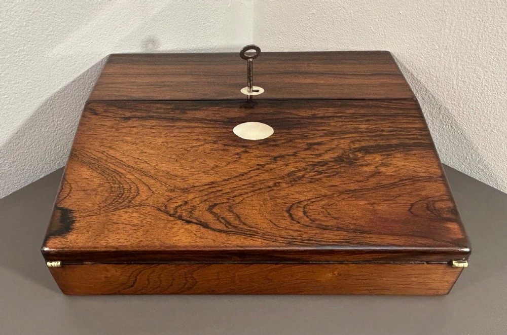 A William IV rosewood lap desk featuring a brass keyhole escutcheon with key inserted and a circular brass inlay on its sloped lid. View X