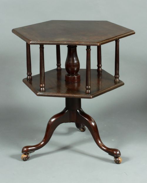 A dark mahogany two-tiered hexagonal dumb waiter table featuring turned vertical spindles, a central pedestal stem, cabriole tripod legs, and castors.