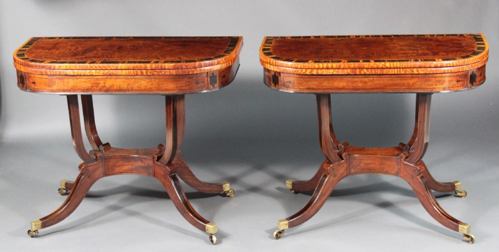 A matching three-piece Regency period furniture set featuring a central sofa table with drawers flanked by a pair of D-shaped folding card tables, all crafted with figured wood and crossbanded inlay borders on curved legs with brass castors. View II