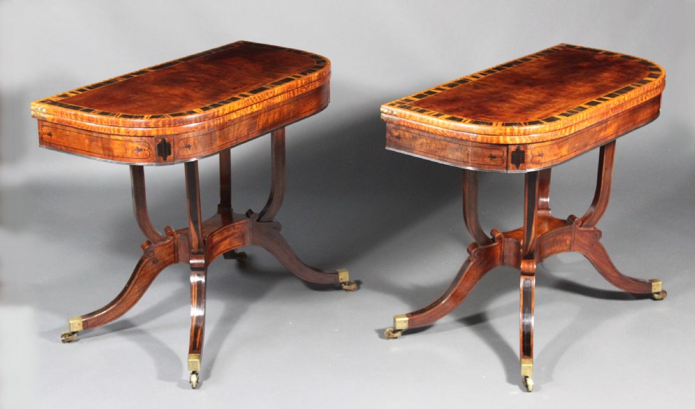 A matching three-piece Regency period furniture set featuring a central sofa table with drawers flanked by a pair of D-shaped folding card tables, all crafted with figured wood and crossbanded inlay borders on curved legs with brass castors. View III