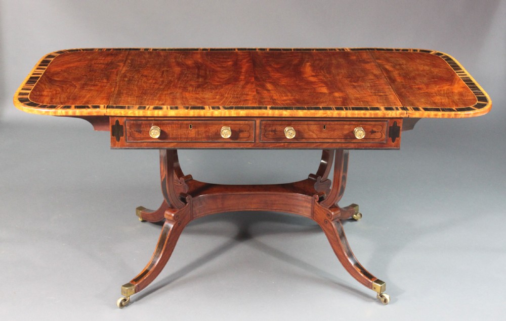 A matching three-piece Regency period furniture set featuring a central sofa table with drawers flanked by a pair of D-shaped folding card tables, all crafted with figured wood and crossbanded inlay borders on curved legs with brass castors. View IV