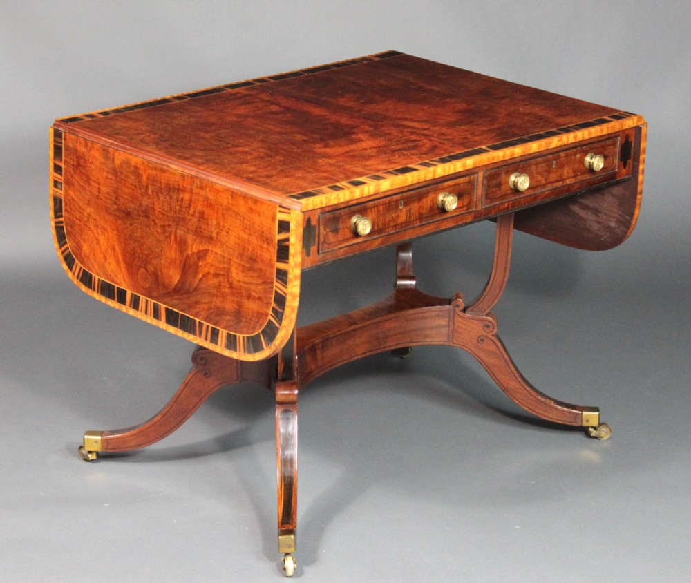A matching three-piece Regency period furniture set featuring a central sofa table with drawers flanked by a pair of D-shaped folding card tables, all crafted with figured wood and crossbanded inlay borders on curved legs with brass castors. View VI