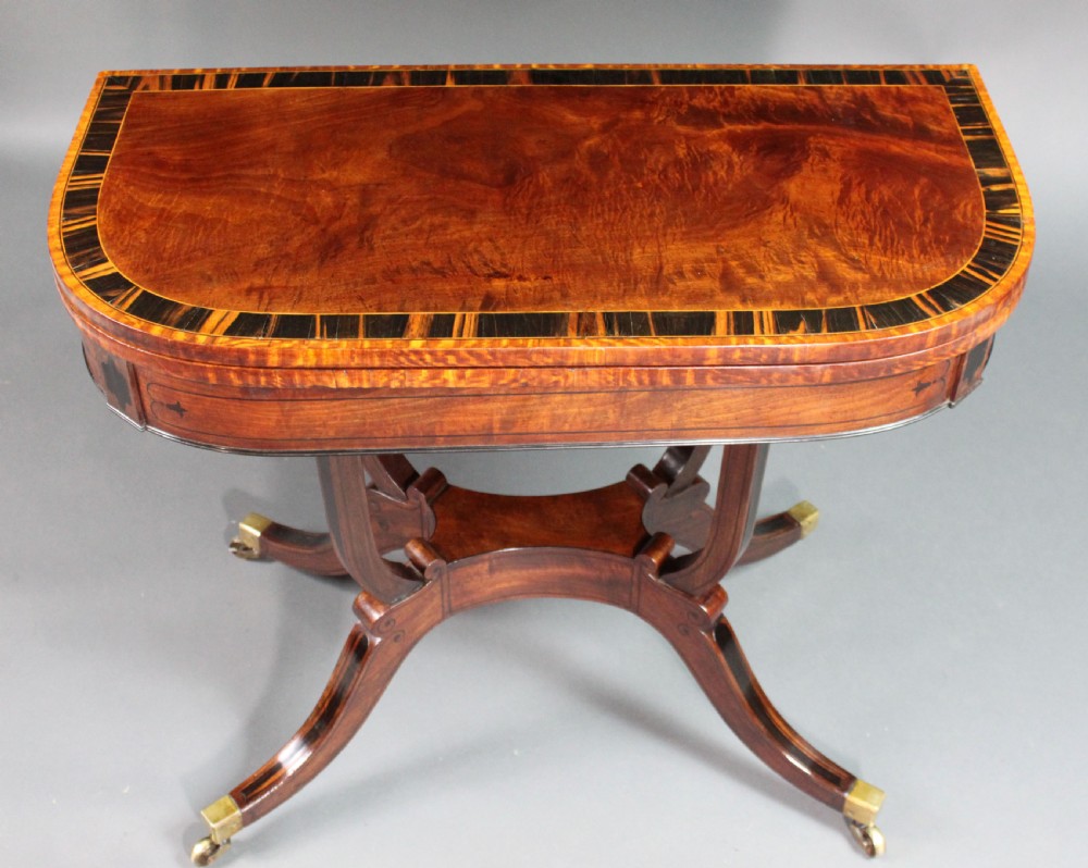 A matching three-piece Regency period furniture set featuring a central sofa table with drawers flanked by a pair of D-shaped folding card tables, all crafted with figured wood and crossbanded inlay borders on curved legs with brass castors. View VIII