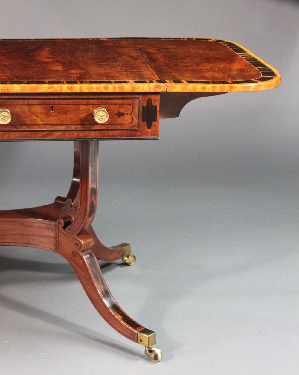 A matching three-piece Regency period furniture set featuring a central sofa table with drawers flanked by a pair of D-shaped folding card tables, all crafted with figured wood and crossbanded inlay borders on curved legs with brass castors. View XV