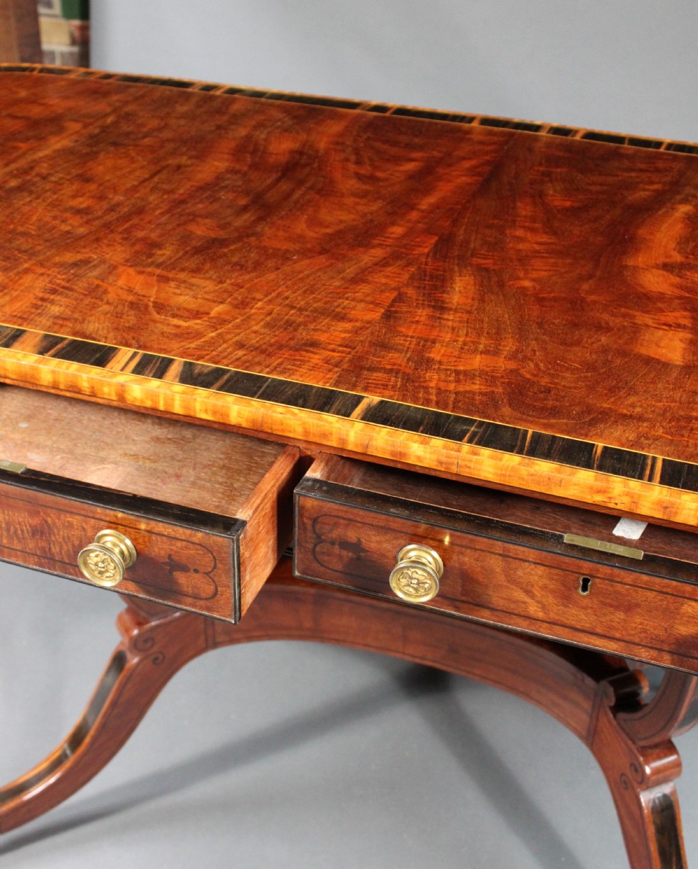 A matching three-piece Regency period furniture set featuring a central sofa table with drawers flanked by a pair of D-shaped folding card tables, all crafted with figured wood and crossbanded inlay borders on curved legs with brass castors. View XVI