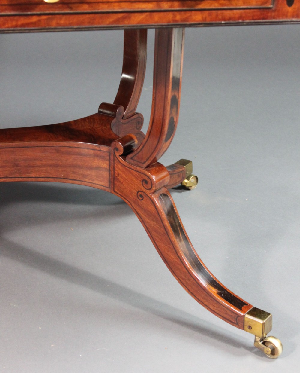 A matching three-piece Regency period furniture set featuring a central sofa table with drawers flanked by a pair of D-shaped folding card tables, all crafted with figured wood and crossbanded inlay borders on curved legs with brass castors. View XVIII