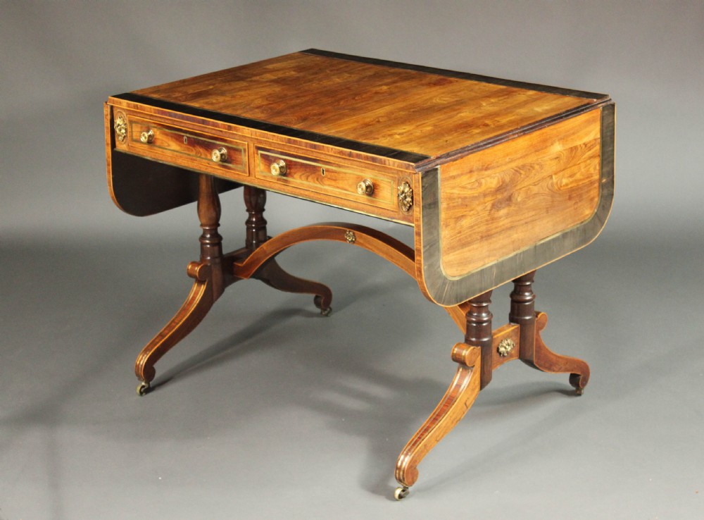 A Regency period kingwood sofa table with brass inlay, two drawers, drop-leaf sides, turned legs, an arched stretcher, and brass castors. View II