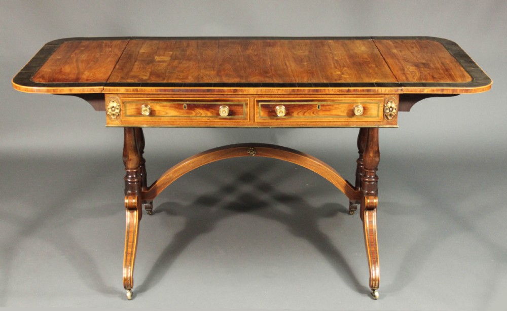 A Regency period kingwood sofa table with brass inlay, two drawers, drop-leaf sides, turned legs, an arched stretcher, and brass castors. View III