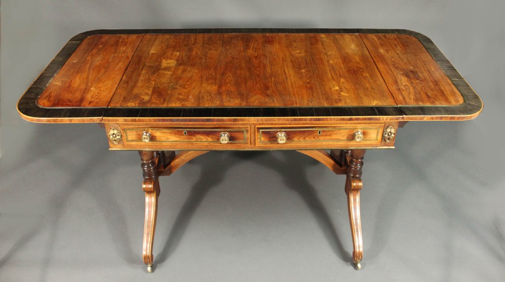 A Regency period kingwood sofa table with brass inlay, two drawers, drop-leaf sides, turned legs, an arched stretcher, and brass castors. View IV