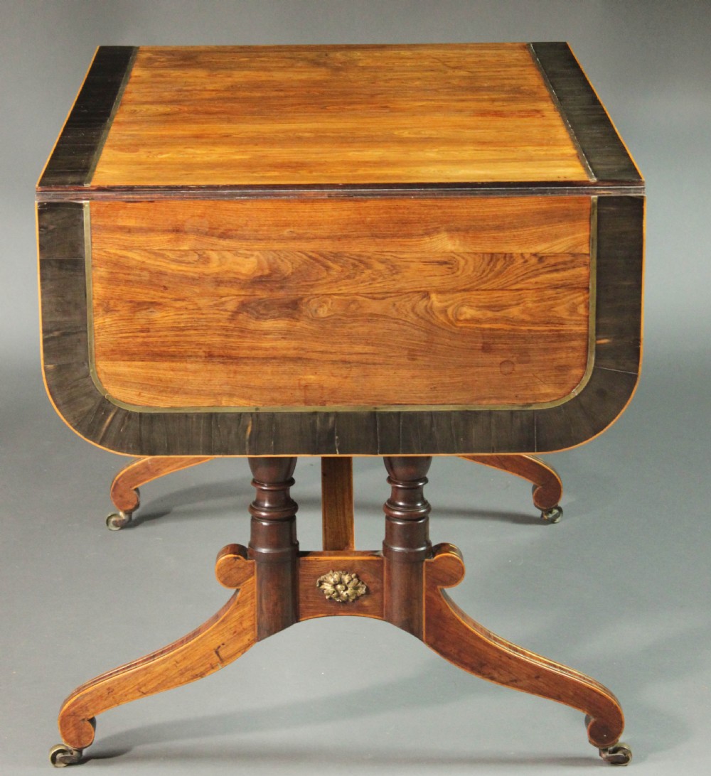 A Regency period kingwood sofa table with brass inlay, two drawers, drop-leaf sides, turned legs, an arched stretcher, and brass castors. View V