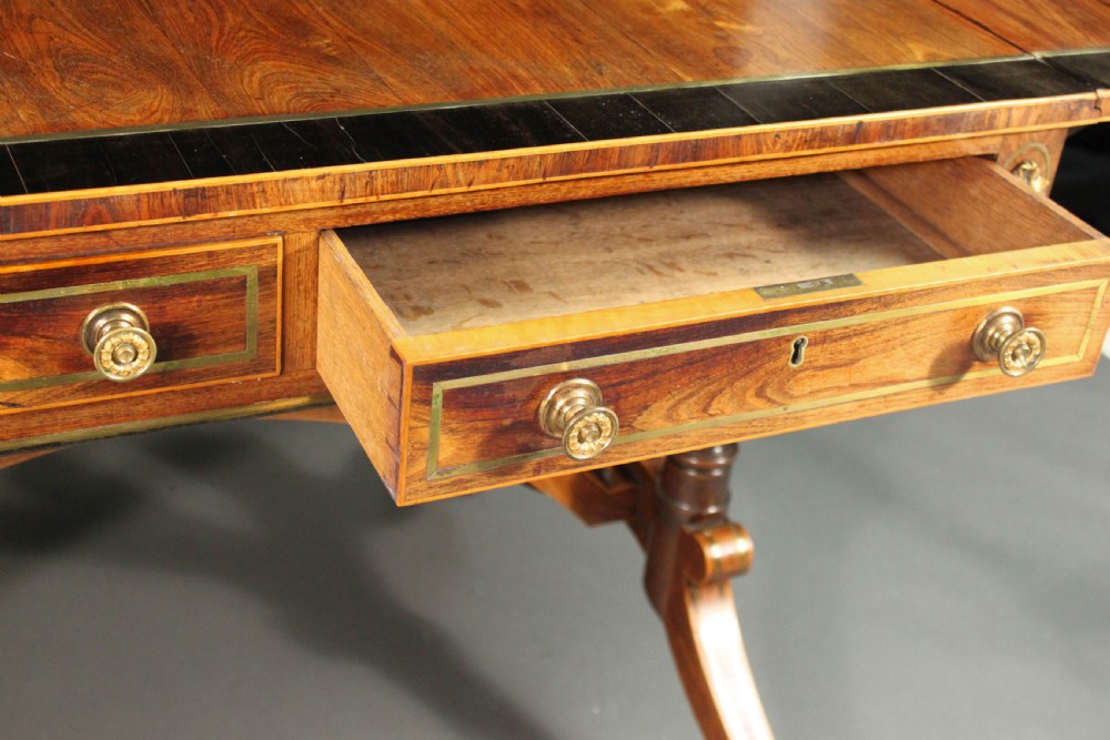 A Regency period kingwood sofa table with brass inlay, two drawers, drop-leaf sides, turned legs, an arched stretcher, and brass castors. View VI
