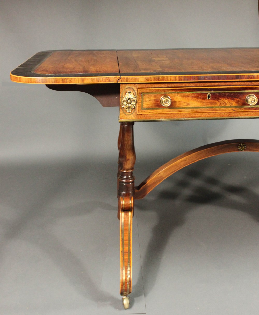 A Regency period kingwood sofa table with brass inlay, two drawers, drop-leaf sides, turned legs, an arched stretcher, and brass castors. View VII